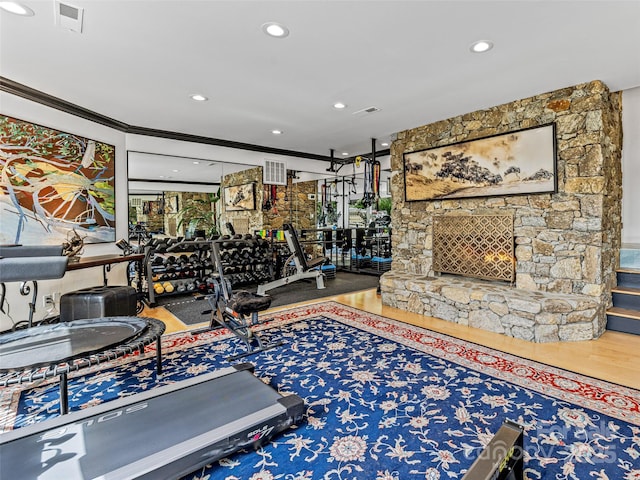 exercise room featuring ornamental molding, a stone fireplace, wood finished floors, and visible vents