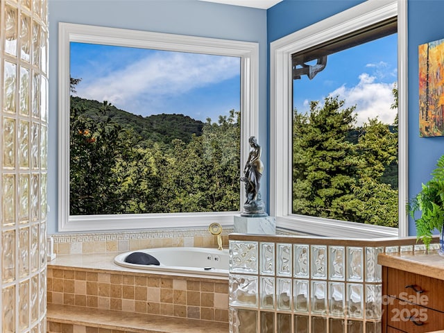 bathroom with a view of trees, vanity, a bath, and a healthy amount of sunlight