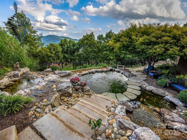 view of yard featuring fence, a mountain view, and a garden pond