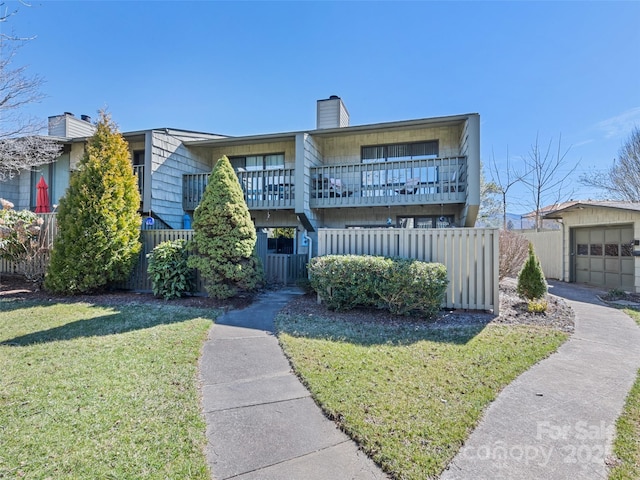 townhome / multi-family property with a balcony, a garage, fence, a front lawn, and a chimney