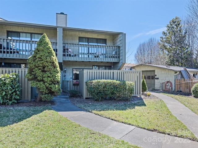 multi unit property featuring a balcony, a chimney, fence, and a front yard