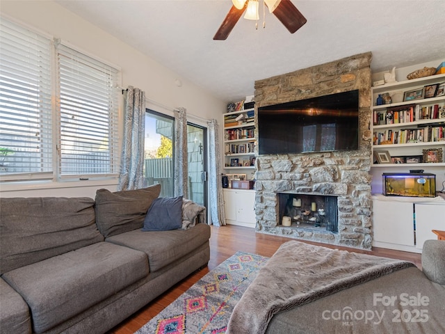 living area with ceiling fan, a stone fireplace, and wood finished floors