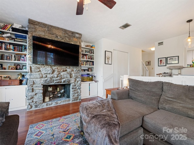 living area featuring a ceiling fan, visible vents, a stone fireplace, and wood finished floors