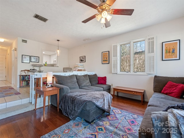 living room featuring dark wood-style floors, a ceiling fan, visible vents, and a textured ceiling