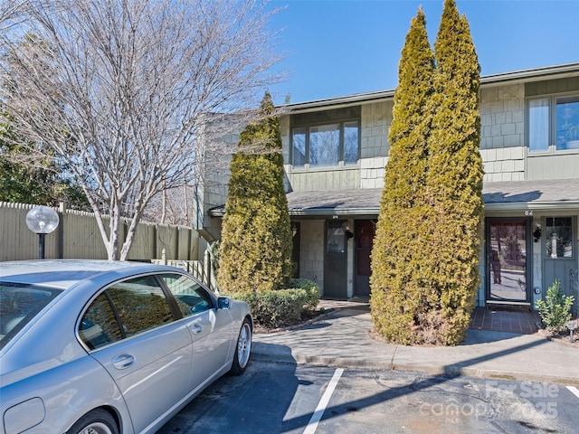 townhome / multi-family property with uncovered parking, fence, and roof with shingles