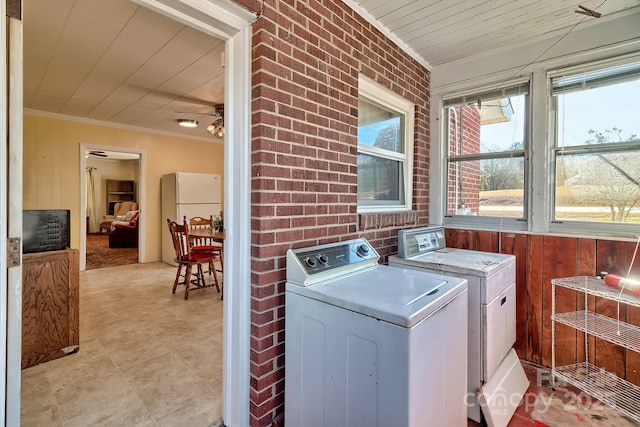 clothes washing area featuring laundry area, wooden walls, washer and clothes dryer, brick wall, and crown molding