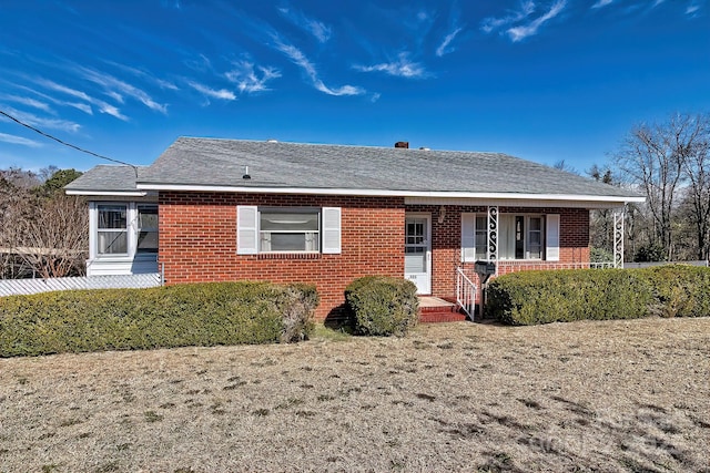 ranch-style home with covered porch, brick siding, and a shingled roof