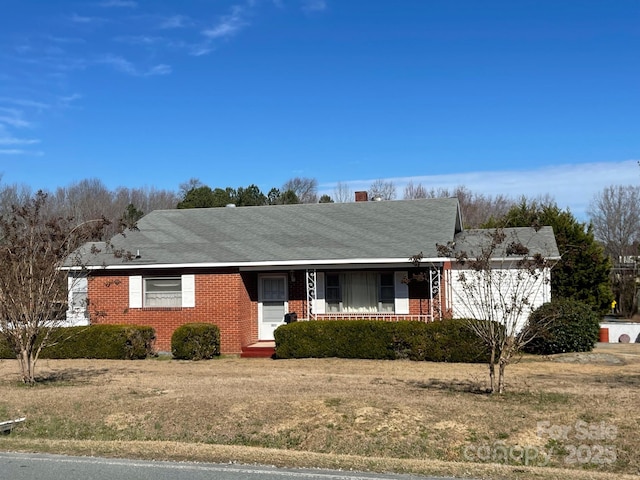 ranch-style home with covered porch, a shingled roof, and brick siding