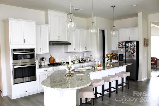 kitchen featuring a center island with sink, visible vents, appliances with stainless steel finishes, white cabinetry, and under cabinet range hood