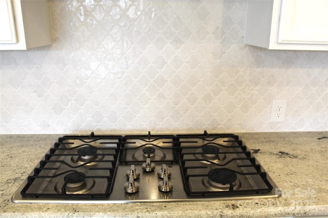 interior details with wallpapered walls, light stone countertops, white cabinets, and stainless steel gas stovetop