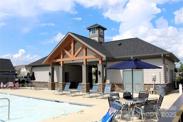 back of property featuring a community pool, a shingled roof, fence, stone siding, and a patio area