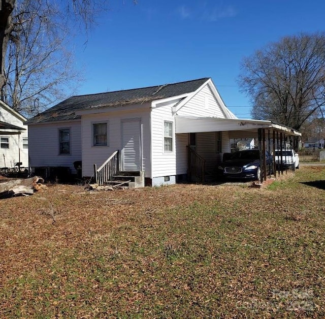 back of house with entry steps, a lawn, and a carport