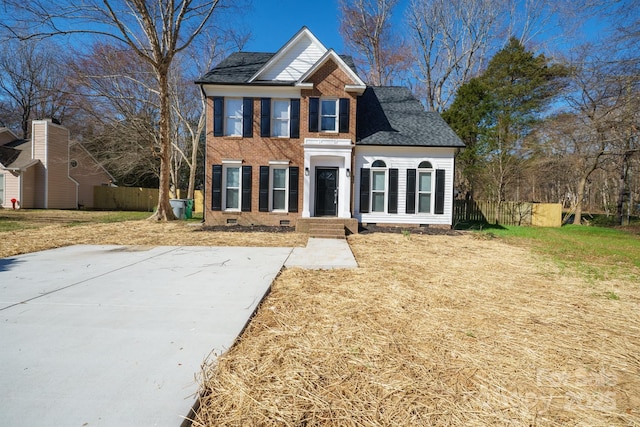 colonial home with crawl space, brick siding, fence, and roof with shingles