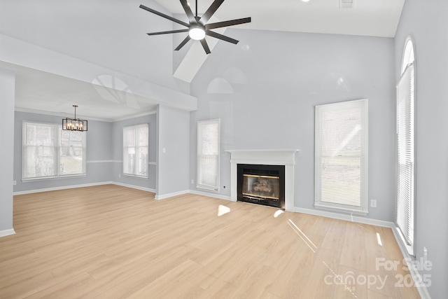 unfurnished living room featuring high vaulted ceiling, ceiling fan with notable chandelier, baseboards, light wood-type flooring, and a glass covered fireplace