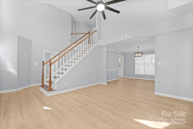 unfurnished living room featuring light wood-style flooring, stairway, baseboards, and ceiling fan with notable chandelier