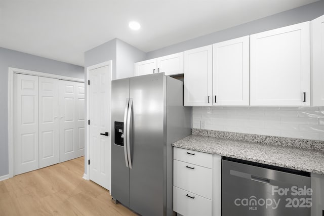 kitchen featuring appliances with stainless steel finishes, backsplash, light stone countertops, and white cabinets