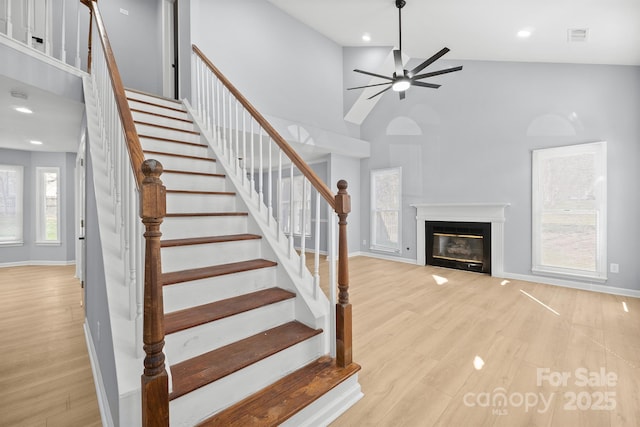 staircase featuring baseboards, visible vents, a glass covered fireplace, a towering ceiling, and wood finished floors