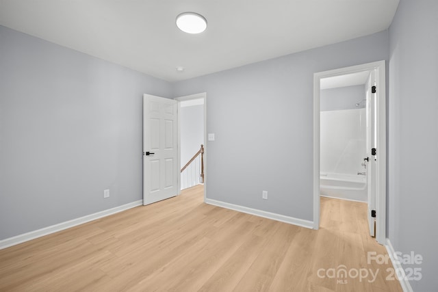 unfurnished bedroom with light wood-type flooring, baseboards, and ensuite bathroom