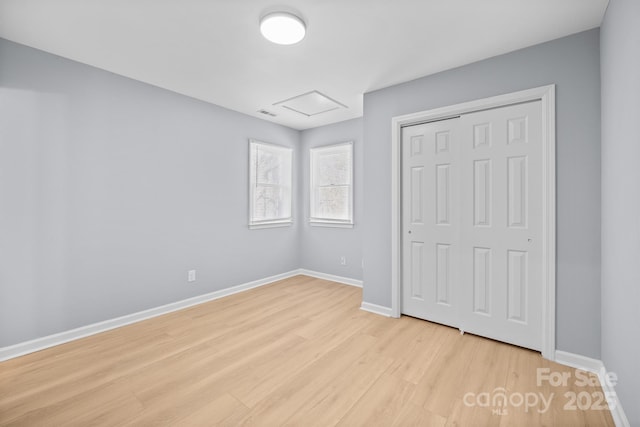 unfurnished bedroom featuring attic access, a closet, light wood-style flooring, and baseboards