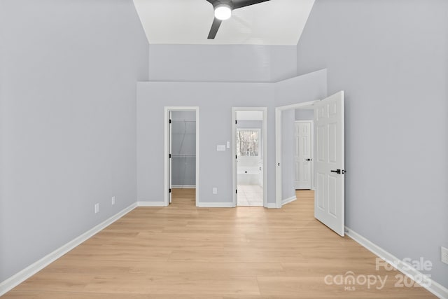 unfurnished bedroom featuring baseboards, a ceiling fan, light wood-style flooring, a walk in closet, and a closet