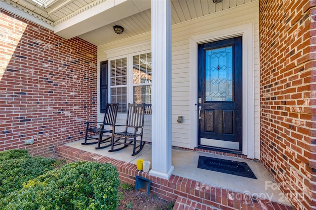 doorway to property with covered porch and brick siding