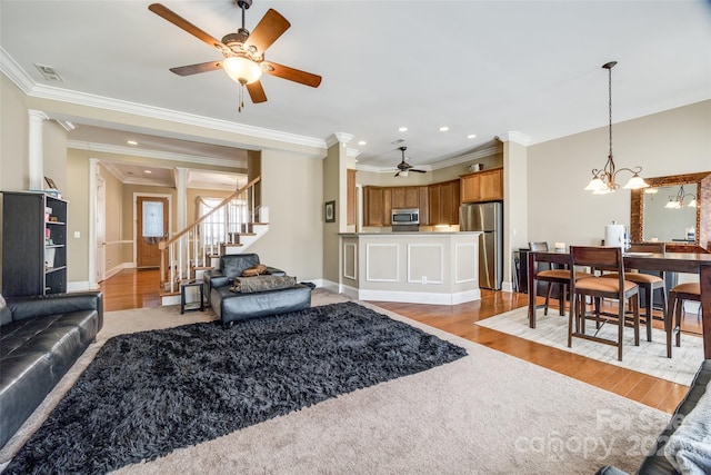 living room featuring ornamental molding, visible vents, light wood finished floors, and stairs