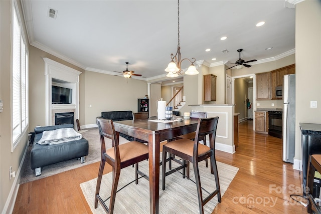 dining space featuring crown molding, visible vents, a fireplace, and light wood finished floors