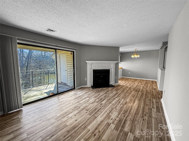 unfurnished living room featuring a fireplace with flush hearth, wood finished floors, visible vents, and baseboards