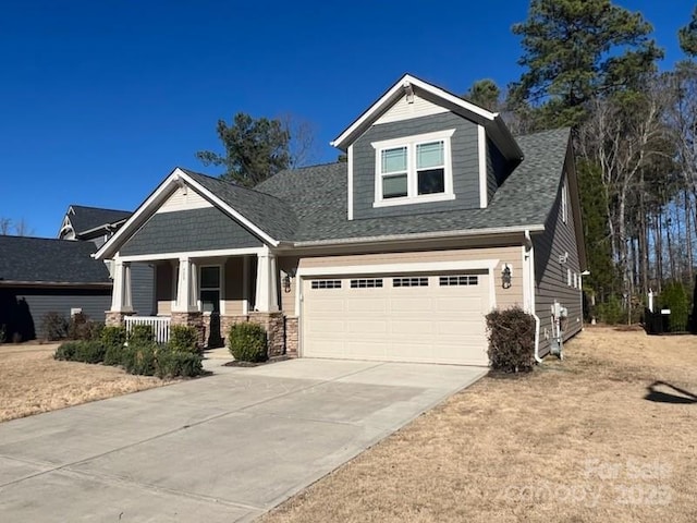 craftsman-style home with covered porch, roof with shingles, and concrete driveway