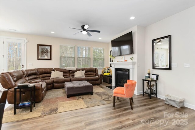 living room featuring light wood finished floors, a fireplace with flush hearth, visible vents, and recessed lighting