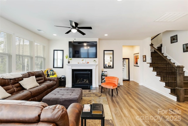 living room featuring recessed lighting, visible vents, a glass covered fireplace, wood finished floors, and stairs