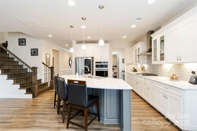 kitchen featuring a breakfast bar area, stainless steel appliances, visible vents, light wood-style floors, and wall chimney exhaust hood