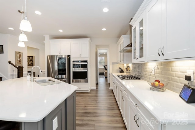 kitchen with light countertops, backsplash, appliances with stainless steel finishes, a sink, and wood finished floors