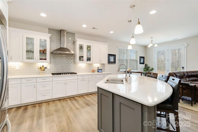 kitchen with a breakfast bar, light countertops, a sink, and wall chimney exhaust hood