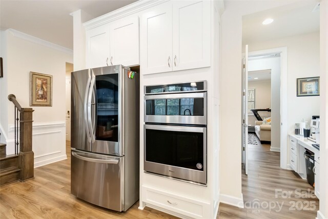 kitchen with appliances with stainless steel finishes, light wood-type flooring, white cabinetry, and crown molding