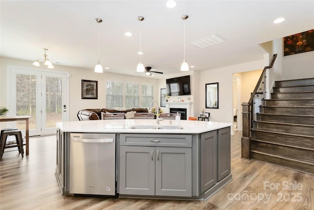 kitchen with gray cabinets, light countertops, open floor plan, a sink, and dishwasher