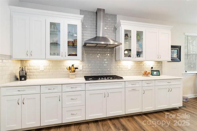 kitchen with gas cooktop, dark wood-style flooring, white cabinets, light countertops, and wall chimney exhaust hood