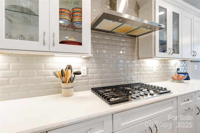 kitchen featuring tasteful backsplash, white cabinets, glass insert cabinets, range hood, and stainless steel gas cooktop