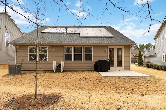 back of property with a shingled roof, cooling unit, roof mounted solar panels, and a patio area