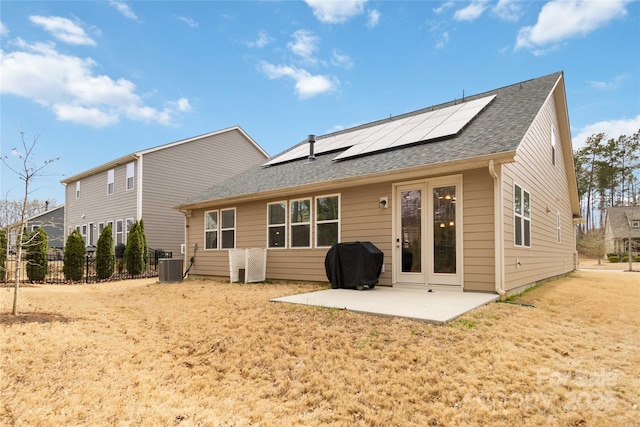 rear view of house with a patio, central AC unit, solar panels, a shingled roof, and fence