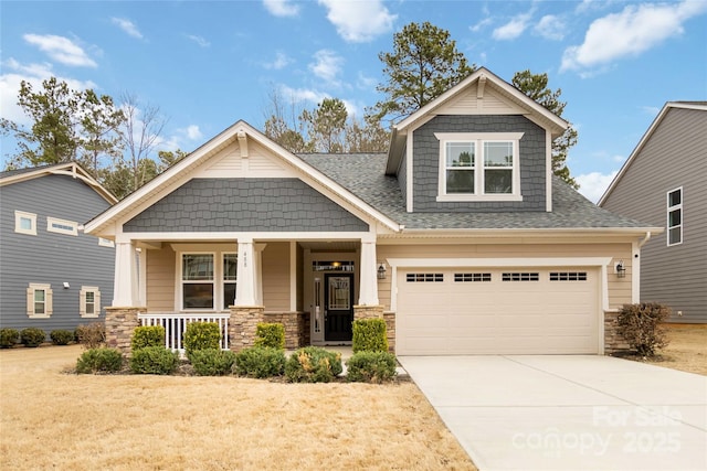 craftsman-style house featuring roof with shingles, covered porch, concrete driveway, a garage, and stone siding