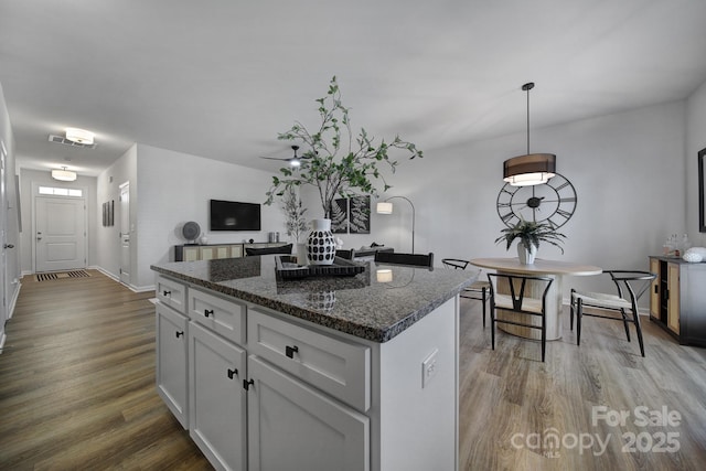 kitchen featuring visible vents, white cabinets, a kitchen island, dark stone countertops, and wood finished floors