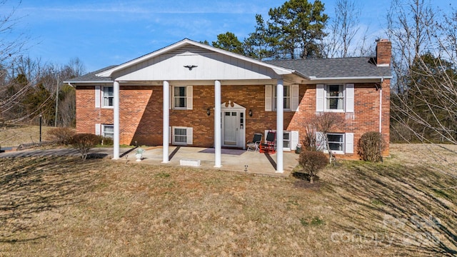 split foyer home with a patio area, brick siding, a chimney, and a front lawn