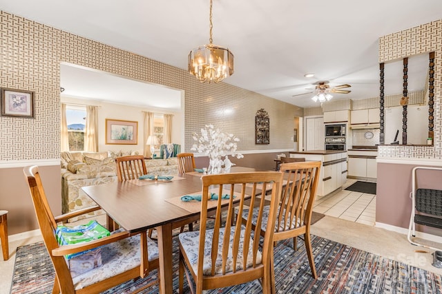 dining space featuring light tile patterned floors, wallpapered walls, and ceiling fan with notable chandelier