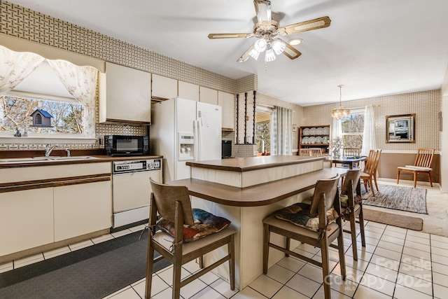 kitchen featuring a wealth of natural light, dark countertops, a sink, white appliances, and wallpapered walls