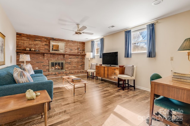 living area featuring light wood-style flooring, a fireplace, visible vents, baseboards, and a ceiling fan