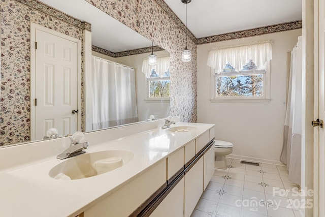 bathroom featuring visible vents, toilet, a sink, baseboards, and wallpapered walls