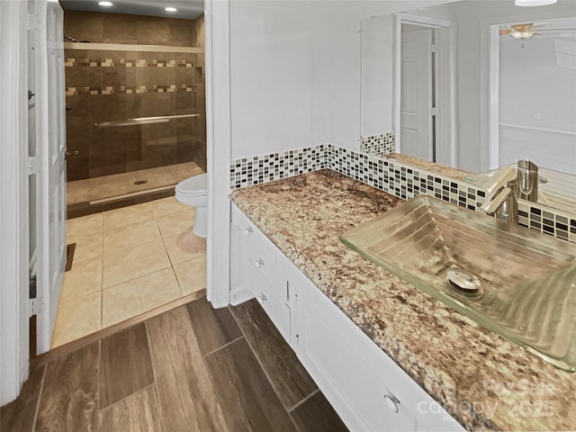 bathroom featuring backsplash, toilet, a ceiling fan, a stall shower, and vanity