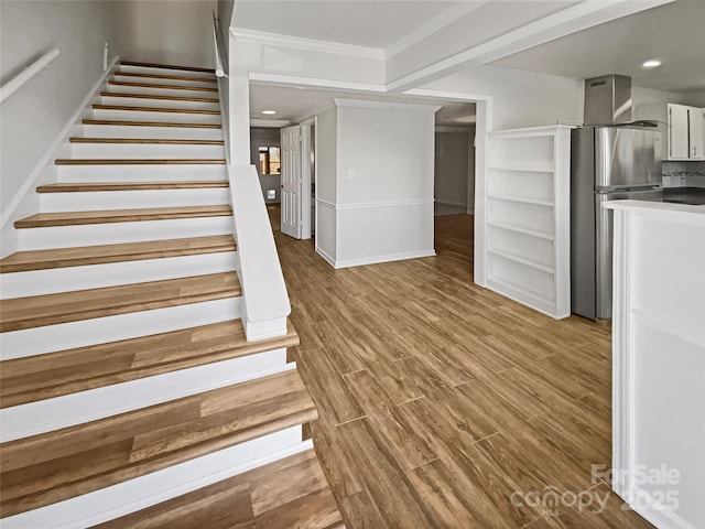 stairs with ornamental molding, wood finished floors, and recessed lighting