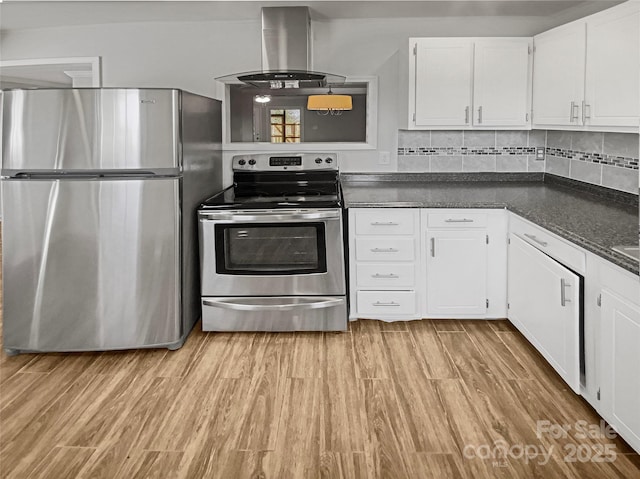 kitchen with light wood-style flooring, appliances with stainless steel finishes, wall chimney range hood, decorative backsplash, and dark countertops